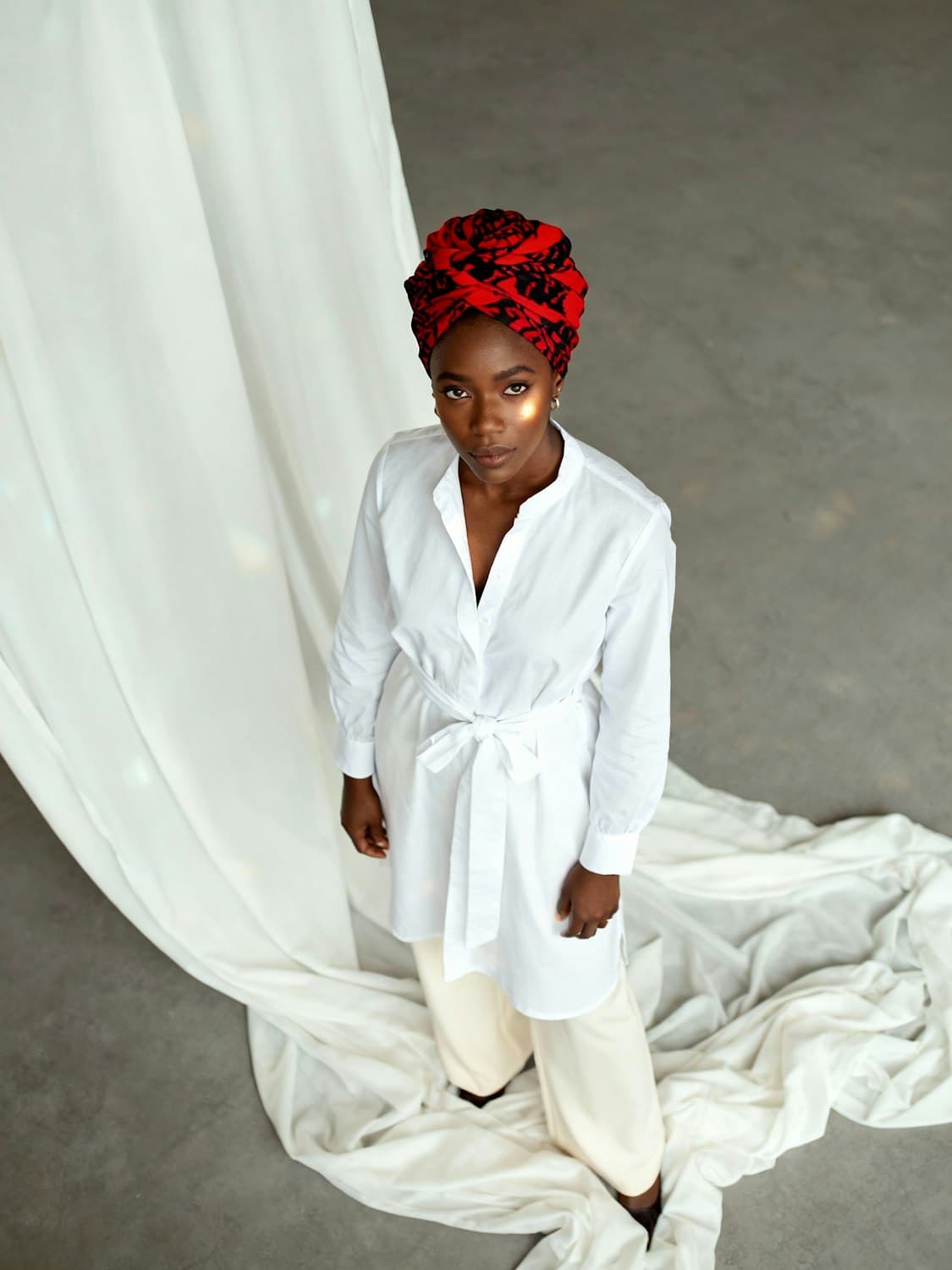 Woman in a white belted shirt tunic, cream wide-leg trousers and a red and black print headwrap