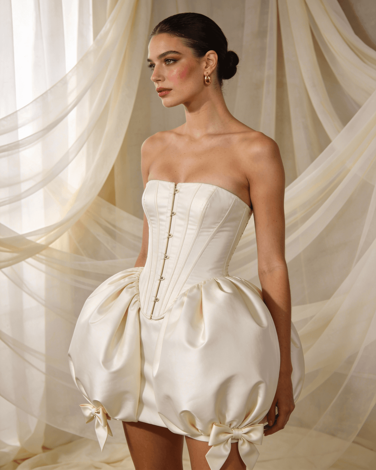 Model in an ivory satin strapless corset dress with a bubble skirt and bows at the hem