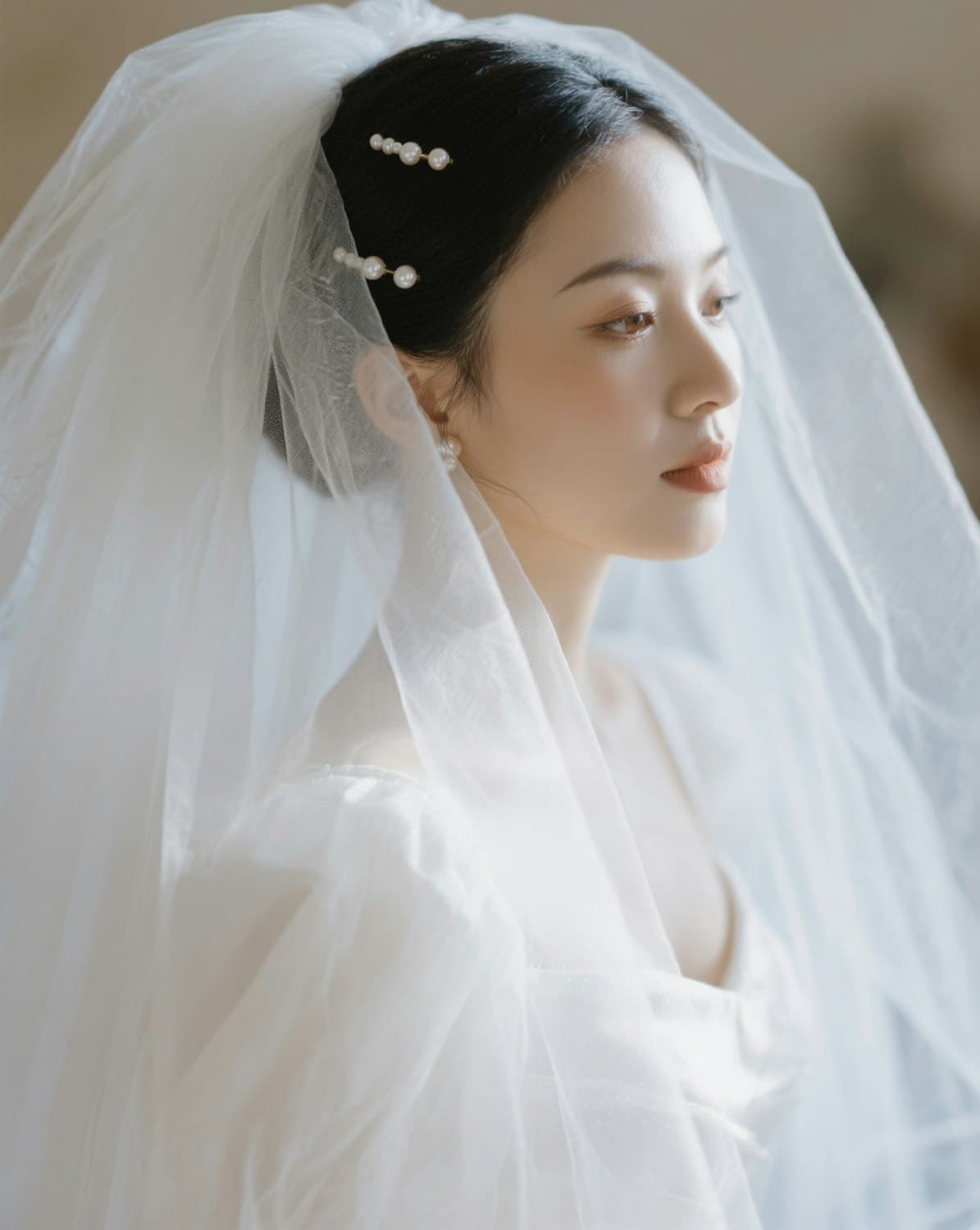 Bride in a white gown with sheer puff sleeves and a long tulle veil, with pearl pins in her hair