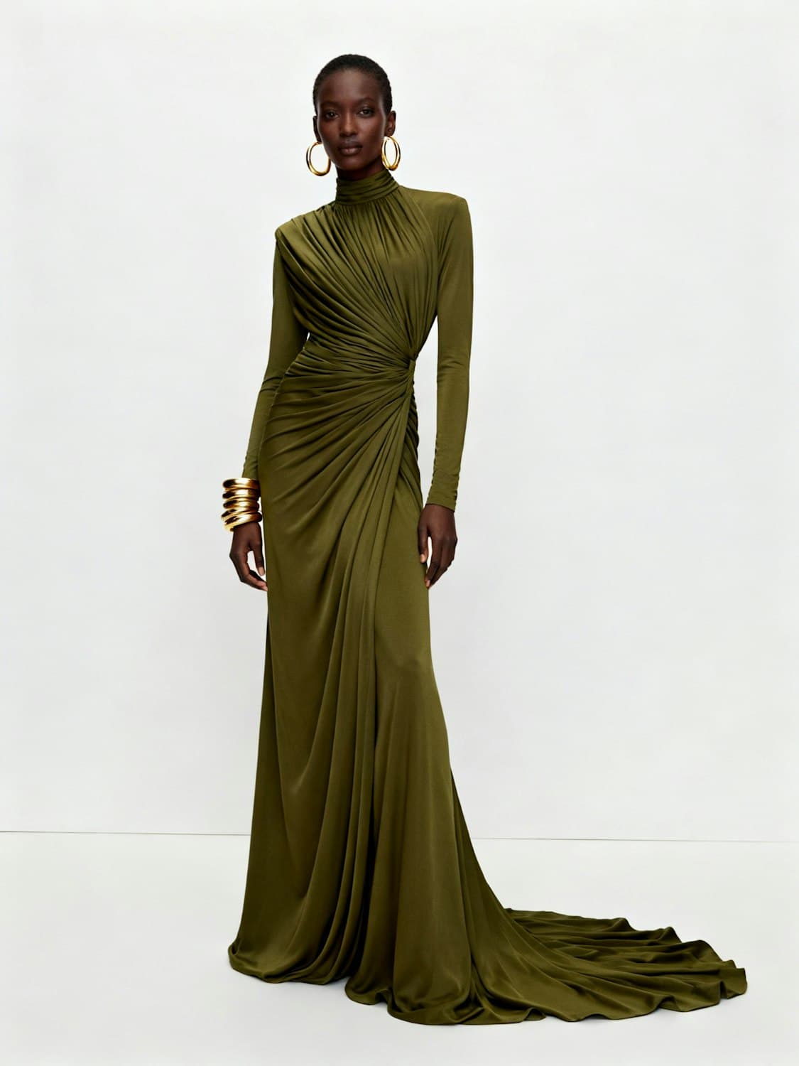 Model in a long olive-green draped gown with long sleeves and gold jewellery